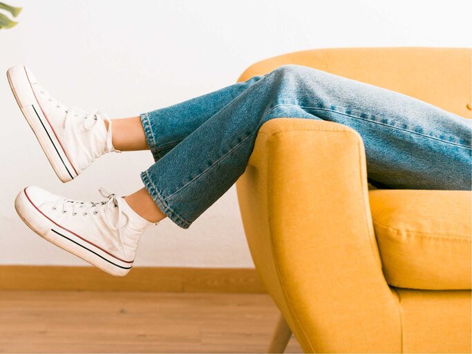 Frau liegt in Jeans auf der Couch. | © Getty Images/Israel Sebastian