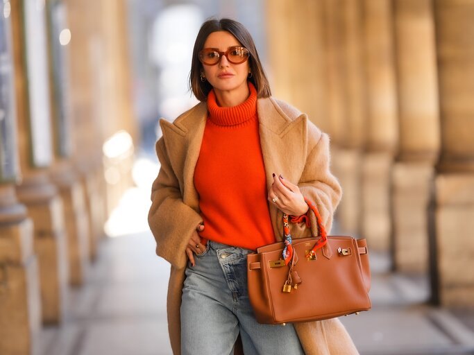 Frau mit beigem Mantel, orangem Rollkragenpullover und blauen Jeans | © Getty Images/Edward Berthelot