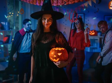 Frau auf Halloween-Party als Hexe verkleidet mit Halloween-Kürbis im Arm. | © Adobe Stock/Gorodenkoff