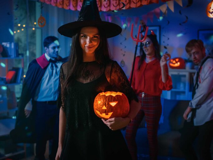 Frau auf Halloween-Party als Hexe verkleidet mit Halloween-Kürbis im Arm. | © Adobe Stock/Gorodenkoff