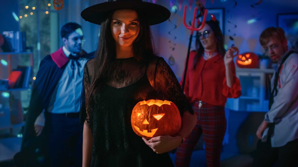 Frau auf Halloween-Party als Hexe verkleidet mit Halloween-Kürbis im Arm. | © Adobe Stock/Gorodenkoff