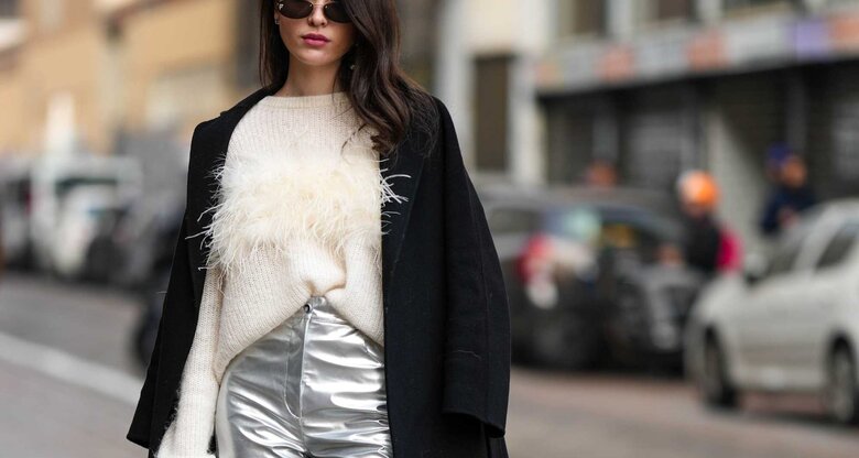 Frau trägt schwarze Sonnenbrille, weißen Wollpullover, schwarzen Mantel und weite silberne Hosen  | © Getty Images/Edward Berthelot 