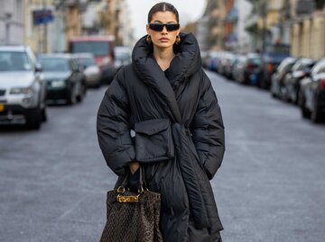 Frau trägt eine lange schwarze Daunenjacke und eine Sonnenbrille | © Getty Images/Christian Vierig