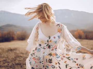 Frau tanzt im Blumenkleid auf Herbstwiese | © Getty Images/South_agency