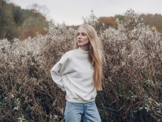 Blonde Frau vor Busch in hellem Pullover | © Getty Images/Igor Ustynskyy