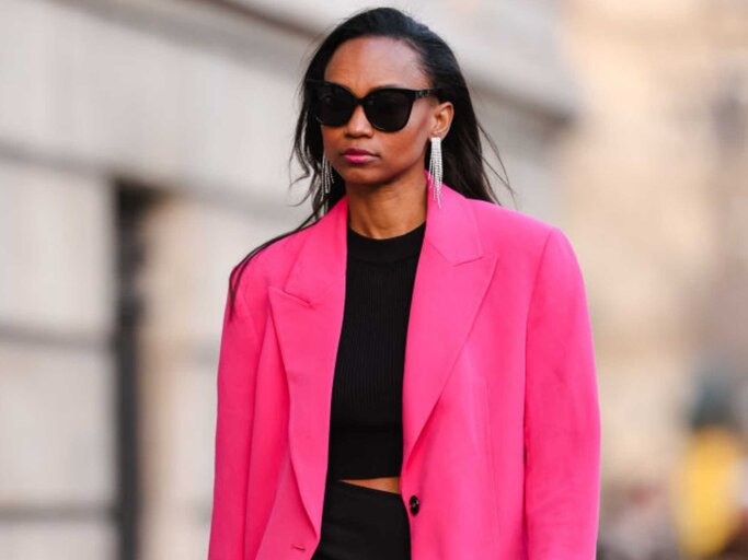 Junge Frau trägt schwarze Sonnenbrille, schwarze Hose, schwarzes Top und oversized Blazer in knallpink.  | © Getty Images/Edward Berthelot 