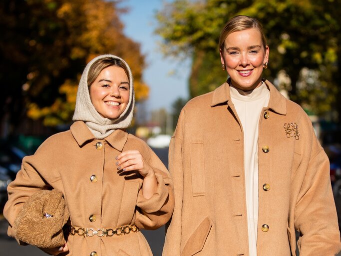 Streetstyle von Amelie Stanescu und Tina Haase in Camel-Mänteln mit Brosche | © Getty Images/Christian Vierig