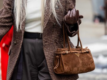 Eine Frau mit langen Haaren trägt eine braune Buckle Bag aus Wildleder. | © Getty Images/Christian Vierig