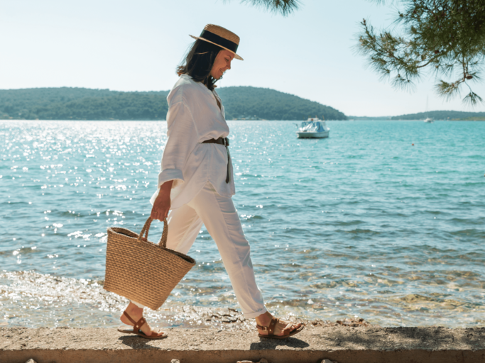 Frau mit Strohtasche geht am Wasser spazieren | © Getty Images/Vera_Petrunina