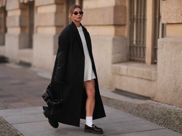 Frau trägt oversized Mantel in Schwarz und ein beiges Strickkleid | © Getty Images/Jeremy Moeller 