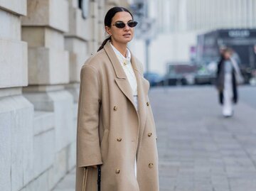 Aufnahme einer Frau in einem beigen Mantel und mit einer Sonnenbrille | © Getty Images/Christian Vierig 