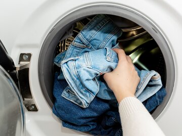 Frau befüllt Waschmaschine mit Jeans | © AdobeStock/Sappheiros