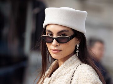 Stilvolle Frau in heller Tweedjacke mit weißer Baskenmütze und schwarzer Sonnenbrille blickt selbstbewusst in die Kamera. | © Getty Images/Raimonda Kulikauskiene