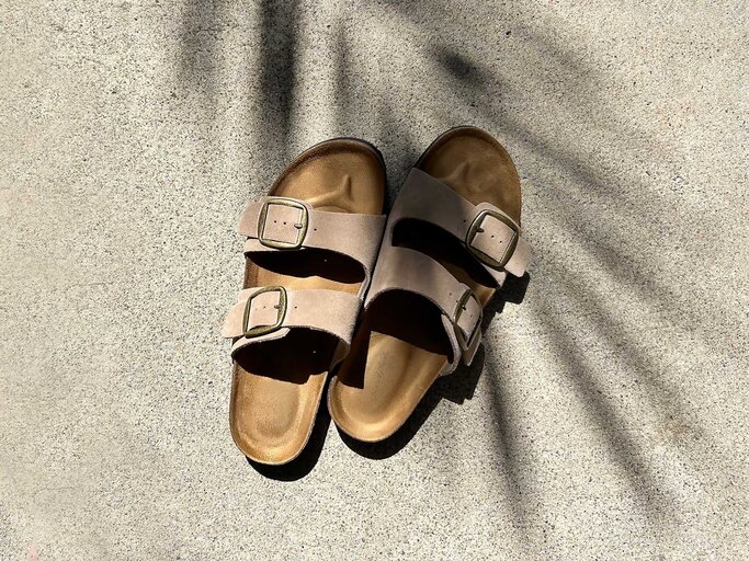 Birkenstock Sandalen in Taupe stehen auf dem Boden. Ein Schatten einer Palme liegt auf ihnen. | © Adobe Stock/Cavan