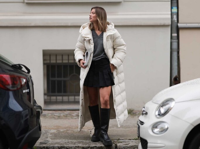 Sophia Geiss trägt einen langen weißen Daunenmantel, einen schwarzen Faltenrock und kniehohe Stiefel. | © Getty Images/Jeremy Moeller