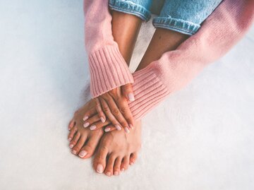 Nahaufnahme von Händen und Füßen mit French Manicure | © Getty Images / Daria Kulkova