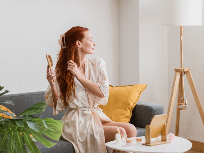 Eine Frau sitzt auf der Couch und bürstet ihre roten langen Haare | © Getty Images / David Espejo