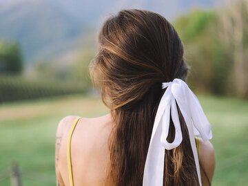 Bild von Frau mit braunen langen Haaren, die mit einer weißen Schleife am Hinterkopf lässige Langhaarfrisur zusammengebunden sind.  | © Getty Images/Elizaveta Starkova