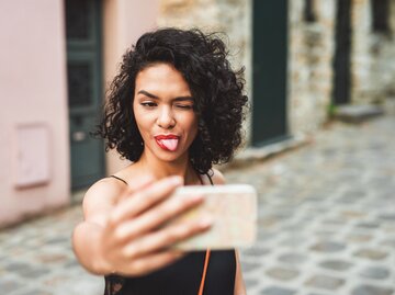 Eine Frau macht ein Selfie mit rausgestreckter Zunge | © Getty Images / Moyo Studio