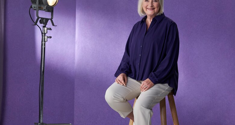 Yvonne Gallo ist eine ältere Dame, die auf einem Hocker sitzt vor einem lila Hintergrund | © Always