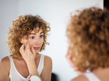 Eine Frau mit Locken trägt sich Creme unter den Augen auf | © Adobe Stock/All king of people