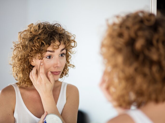 Eine Frau mit Locken trägt sich Creme unter den Augen auf | © Adobe Stock/All king of people