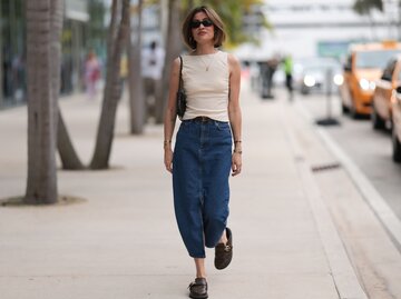 unge Frau mit Sonnenbrille und Bob-Frisur läuft in Jeansrock und Cremetop durch eine Stadtstraße. | © Getty Images/Jeremy Moeller