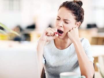 Junge Frau in Büro sitzt gähnend am Schreibtisch vor dem Laptop | © iStock / Neustockimages 