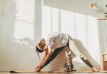 Eine junge Frau macht Yoga, vor ihr sitzt eine Katze. | © GettyImages/Kseniya Ovchinnikova