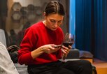 Frau mit einem Glas Rotwein in der Hand tippt auf ihrem Handy | © Getty Images/Rehulian Yevhen