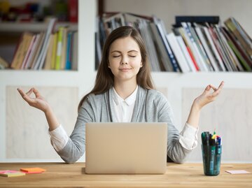 Frau sitzt in Yogapose am Schreibtisch | © iStock | fizkes