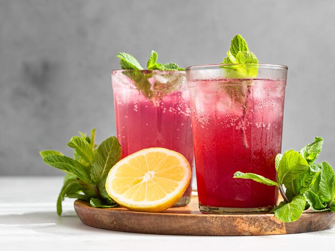 Hibiskuseistee mit Zitrone, Minze und Eis in Gläsern auf grauem Steinhintergrund | © gettyimages.de | porosolka