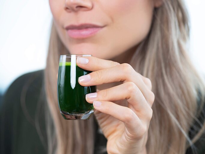 Nahaufnahme von einer Frau, die ein Glas mit Weizengrassaft hält. | © gettyimages.de | simarik