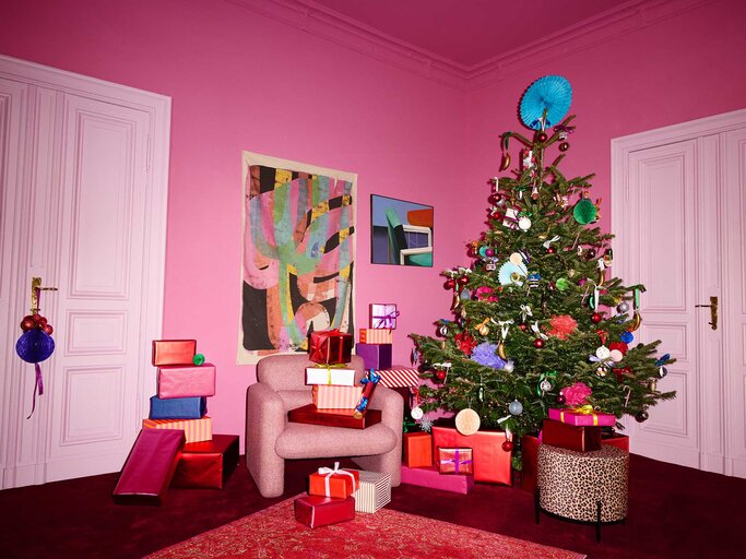 In einem stilvoll pinken Zimmer stehen ein reich geschmückter Weihnachtsbaum, ein Sessel und ein Stapel farbiger Geschenke. | © OTTO