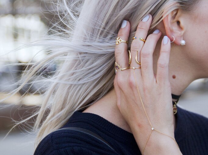 Nahaufnahme einer Frau mit Ohrringen und mehreren Goldringen an der Hand | © Getty Images | Georgie Hunter 