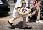  Streetstyle mit weißem Spitzenkleid, Basttasche mit bunten Bommeln und schwarzen Mules mit Straß-Detail auf der Mailänder Menswear Fashion Week | © Getty Images / Christian Vierig