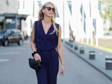 Blonde Frau mit Sonnenbrille trägt Street Style mit weiß gepunktetem Jumpsuit in Marineblau in Kopenhagen | © Getty Images