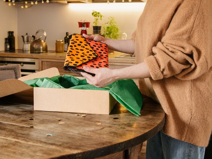 Frau in hellbraunem Pullover packt orange Tasche mit Leopardenmuster aus | © Vinted