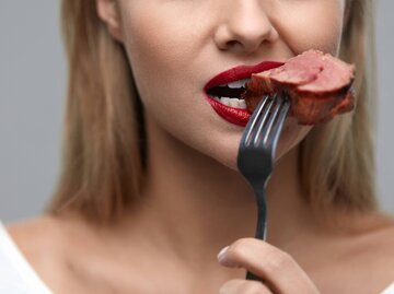 Frau beißt in ein Stück Fleisch | © iStock | puhhha