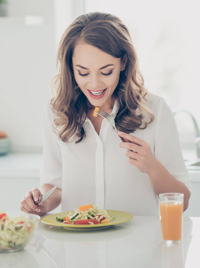 Frau isst  einen Salat am Tisch sitzend | © iStock | Deagreez