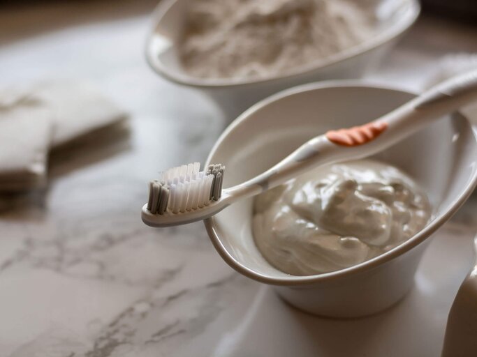 Zahnbürste liegt auf Porzellanschale mit weißer Paste, die auf Marmorplatte steht | © iStock | istockphotoluis