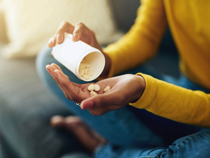 Frau sitzt im Schneidersitz und schüttet sich Nahrungsergänzungsmittel Pillen aus einer Dose auf die Hand | © iStock | Jay Yuno