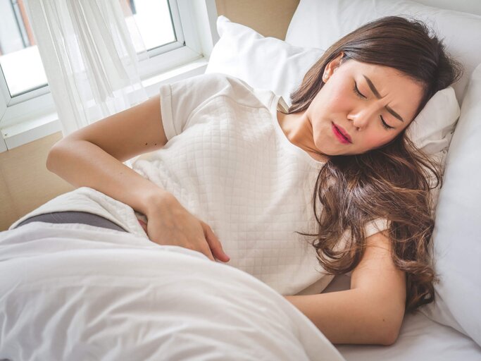 Junge asiatische Frau liegt im Bett und hat Schmerzen aufgrund einer Blasenentzündung. | © iStock | Nattakorn Maneerat