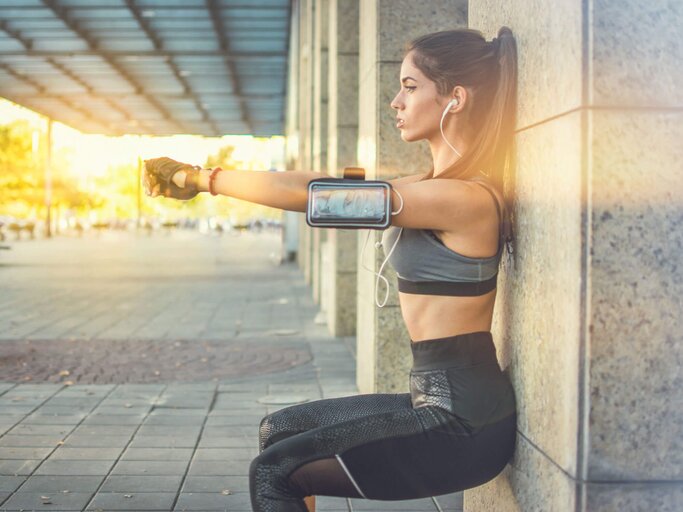 Junge Frau im Sportoutfit befindet sich in der Wandhocke und übt Bauch-Beine-Po-Training. | © iStock | Bojan89