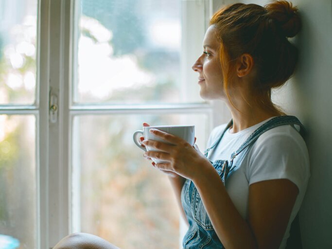 Frau sitzt auf der Fensterbank und denkt nach. | © iStock | Jasmina007