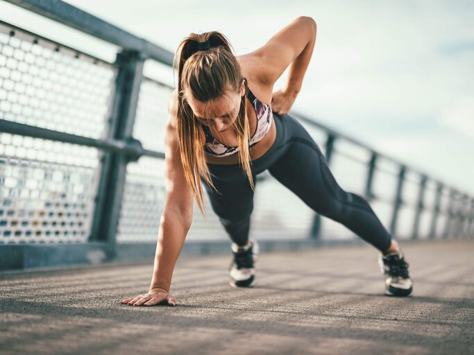 Frau macht einarmige Liegestütze auf einer Brücke. | © iStock | MilanMarkovic