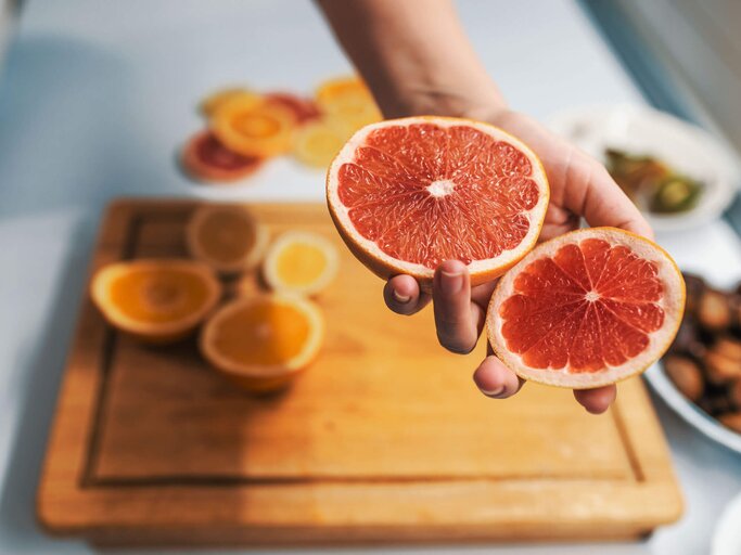 Frauenhand hält eine aufgeschnittene Grapefruit. | © iStock | ljubaphoto