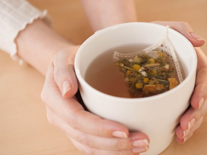 Die Hände einer Frau halten eine Tasse mit Kamillentee umschlossen. | © gettyimages.de / Tetra Images