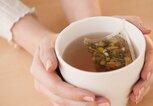 Die Hände einer Frau halten eine Tasse mit Kamillentee umschlossen. | © gettyimages.de / Tetra Images