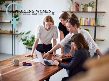 Eine Gruppe von Frauen steht an einem Tisch und schaut auf einen Laptop. | © Getty Images / Oliver Rossi